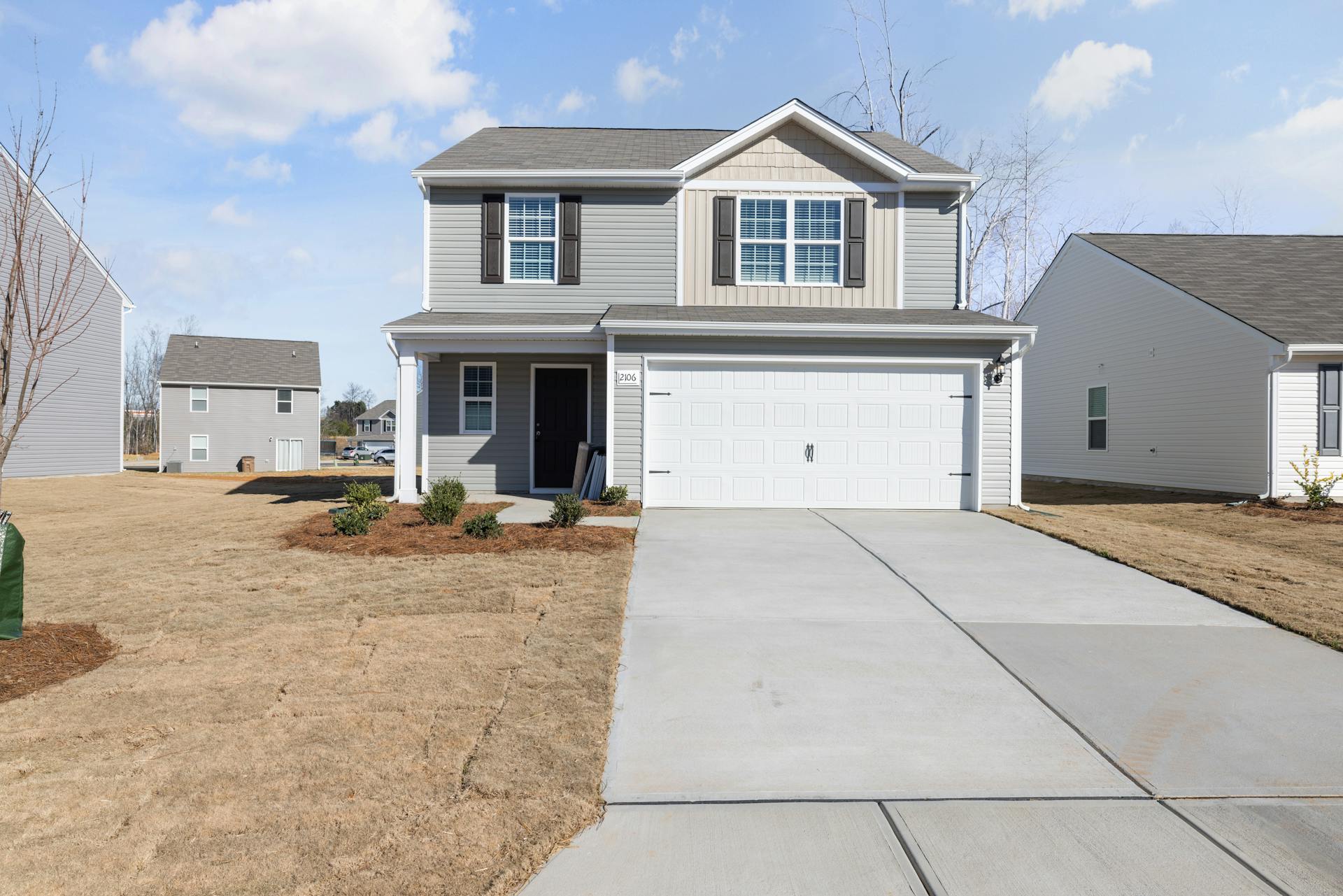 A new two-story home with light gray siding and white trim stands under a clear sky. Its freshly installed landscaping and well-paved driveway present a serene suburban setting. This image reflects the type of property that can instill confidence in first-time homebuyers, especially when inspected by a professional like Val. His ability to make the inspection process straightforward, stress-free, and informative shines through, providing buyers with the clarity and confidence needed to proceed with their purchase